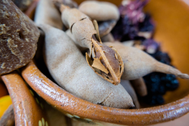 Свежий тамаринд и изюм в глиняной миске рядом с коричневыми сахарными тростями - Фото, изображение