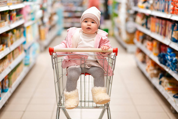 Rodzinne zakupy. Urocze dziecko siedzi w wózku sklepowym w środku supermarketu. Koncepcja zakupów i konsumpcjonizmu. - Zdjęcie, obraz