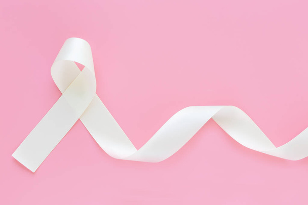 Witte parel lint krullen op roze geïsoleerde achtergrond met kopieerruimte. Longkanker Bewustwording, mesothelioom en Retinoblastoom kanker symbool. Zuiverheidsteken tegen geweld tegen vrouwen, veilig moederschap. - Foto, afbeelding