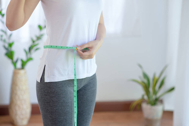 Sportowa kobieta ćwiczy ze zdrowym odżywianiem mierząc swoje szczupłe ciało i cienką talię za pomocą miarki taśmy.  - Zdjęcie, obraz