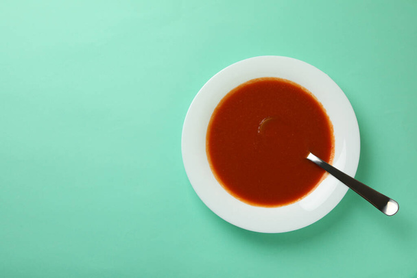 Plate of tasty tomato soup and spoon on mint background - Φωτογραφία, εικόνα