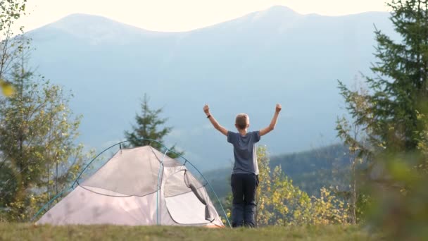 Happy child boy jumping up high with raised hands near a camping tent in mountains enjoying view of beautiful summer nature. Success and active way of life concept. - Footage, Video
