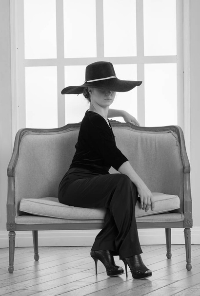 beautiful woman in a big hat sits on the background of the window - Foto, imagen