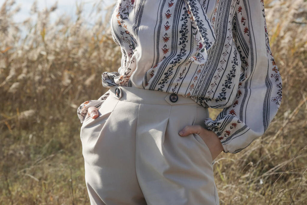 Ritratto di moda all'aperto di donna caucasica in pantaloni beige gamba larga e camicetta fantasia. - Foto, immagini
