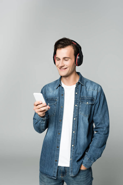 Smiling man in headphones using smartphone isolated on grey - Foto, Imagem