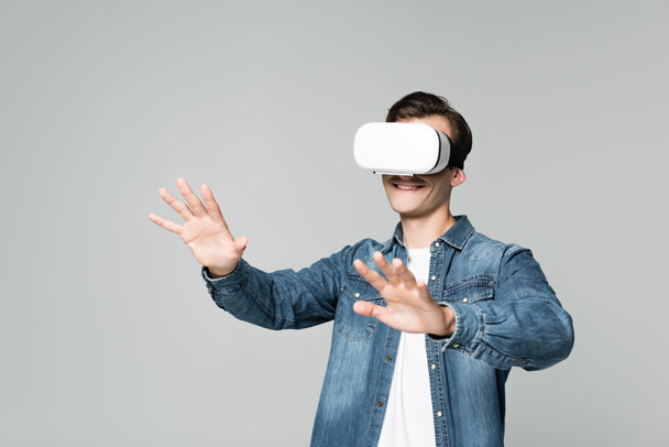 Uśmiechnięty mężczyzna gra wideo w wirtualnej rzeczywistości słuchawki izolowane na szarości - Zdjęcie, obraz