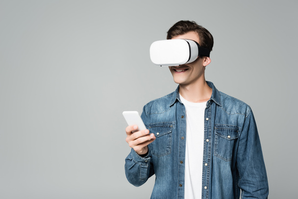 Smiling man vr headset using smartphone isolated on grey - Fotoğraf, Görsel