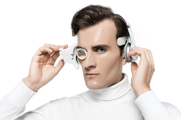 Cyborg při pohledu na fotoaparát při dotyku digitální oční čočky a sluchátka izolované na bílém - Fotografie, Obrázek