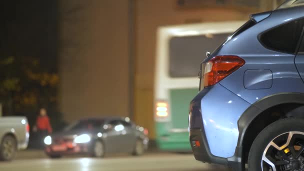 Coche azul estacionado en la calle de la ciudad brillantemente iluminada con semáforos en movimiento en el fondo por la noche. - Imágenes, Vídeo