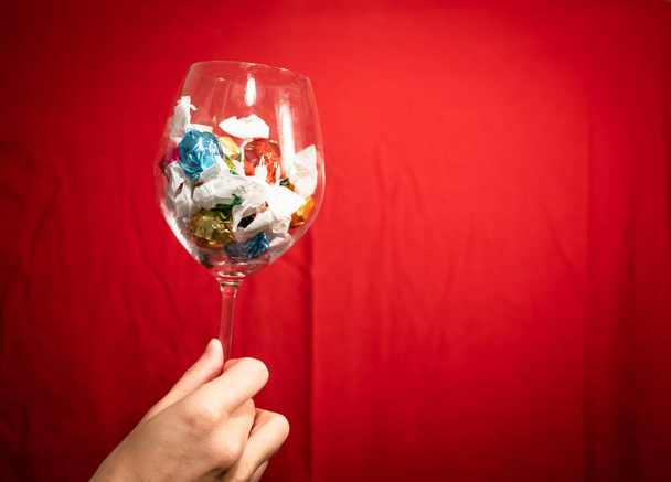 Imagem conceitual de um copo de cristal de mão preenchido com pralinas de chocolate envolto em cores brilhantes e vivas. Natal e feriados. - Foto, Imagem