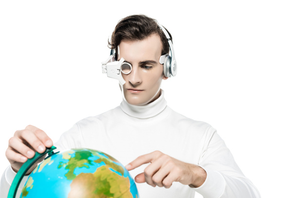Cyborg man in eye lens and headphones pointing with finger at globe on blurred foreground isolated on white - Photo, Image