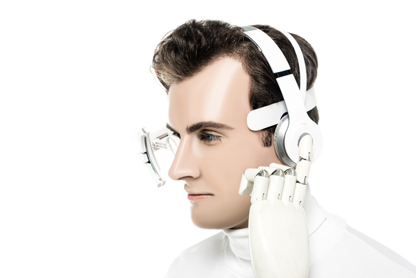 Cyborg in eye lens touching headphones with artificial hand isolated on white - Photo, Image
