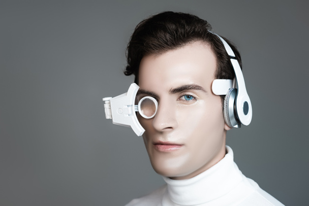 Cyborg in headphones and eye lens looking at camera isolated on grey - Foto, Imagem
