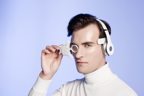 Cyborg ve sluchátkách a oční čočce při pohledu na fotoaparát izolovaný na modré - Fotografie, Obrázek