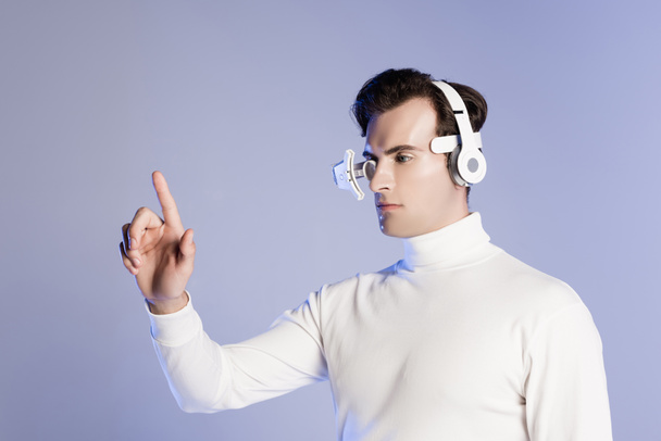 Cyborg in Augenlinse und Kopfhörer berühren etwas Isoliertes auf violett - Foto, Bild