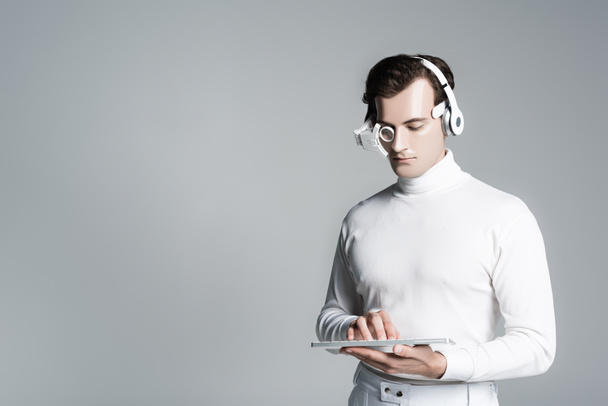 Homem ciborgue em fones de ouvido usando teclado de computador isolado em cinza com espaço de cópia - Foto, Imagem