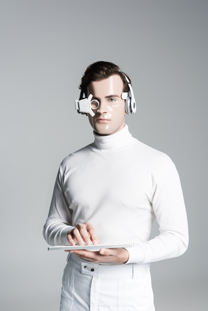 Kulaklıklı Cyborg ve dijital göz merceği bilgisayar klavyesini tutuyor ve gri kameraya bakıyor. - Fotoğraf, Görsel