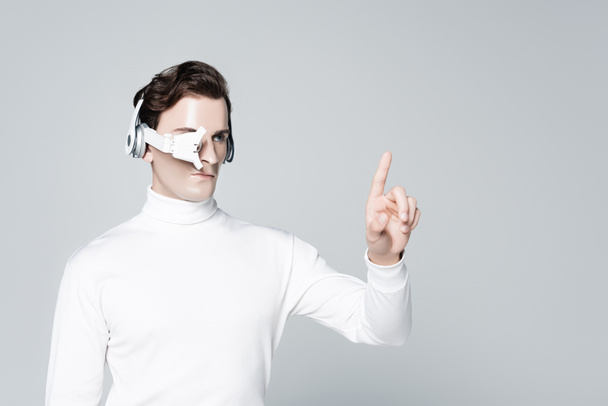 Cyborg in headphones and eye lens pointing with finger isolated on grey - Zdjęcie, obraz