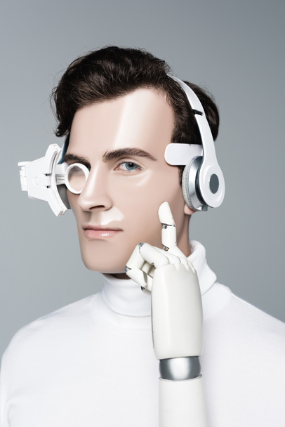 Cyborg im Kopfhörer mit künstlicher Hand blickt auf Kamera isoliert auf grau - Foto, Bild