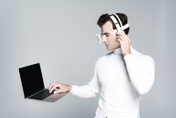Laptop with blank screen in air near cyborg with headphones isolated on grey - Photo, Image