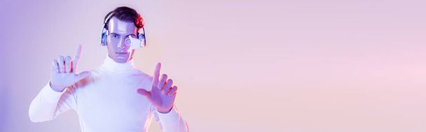 Cyborg en auriculares apuntando con los dedos sobre fondo púrpura, bandera - Foto, Imagen