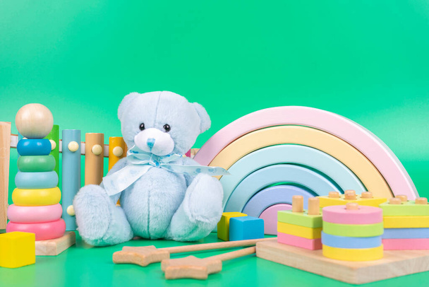 Kids toys collection. Teddy bear, wooden rainbow, educational and music baby toys on light green background - Photo, Image