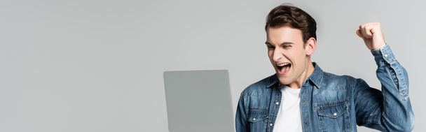 Uomo positivo che mostra sì gesto mentre guarda il computer portatile isolato su grigio, banner - Foto, immagini