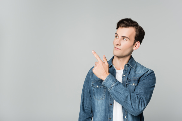 Young man in denim jacket pointing with finger isolated on grey - Fotografie, Obrázek