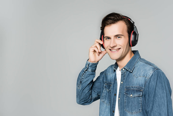 Smiling man in denim jacket and headphones looking at camera isolated on grey - Fotó, kép