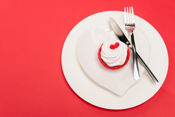 top view of cupcake on plate with cutlery on red background - Фото, изображение