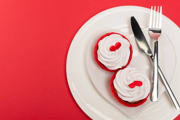 top view of cupcakes on plate with cutlery on red background - Foto, afbeelding