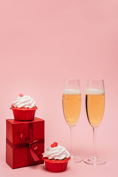 kieliszki szampana w pobliżu prezent i babeczki izolowane na różowy - Zdjęcie, obraz