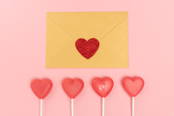 top view of heart shaped lollipops and envelope with heart on pink background - Foto, imagen