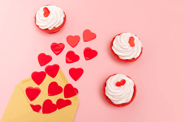 πάνω όψη κόκκινες καρδιές, φάκελος και cupcakes σε ροζ - Φωτογραφία, εικόνα