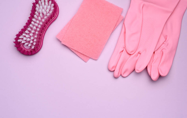 Ροζ λαστιχένια γάντια καθαρισμού, ροζ σφουγγάρια, βούρτσες σε μωβ φόντο, επίπεδο lay - Φωτογραφία, εικόνα