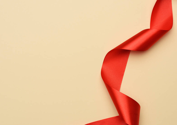 curled red silk ribbon on a beige background, copy space - Фото, зображення