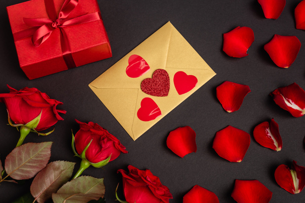 top view of roses, valentines gift and envelope isolated on black - Φωτογραφία, εικόνα