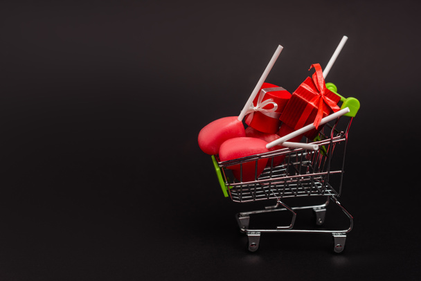 shopping cart with valentines gifts and lollipops isolated on black - Photo, Image