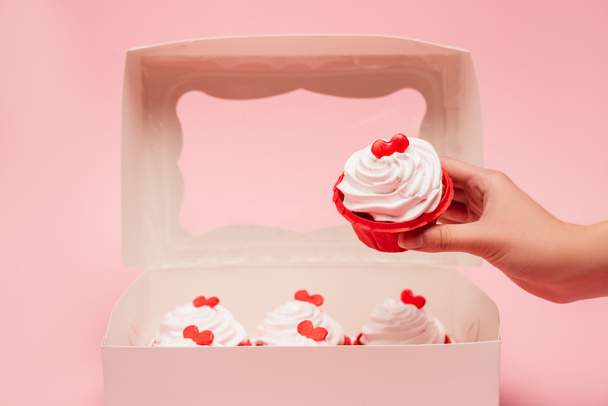 vue recadrée de femme tenant cupcake Valentines près de la boîte sur fond rose - Photo, image