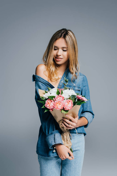 charming woman in denim shirt, with naked shoulder, posing with bouquet isolated on grey - Photo, Image