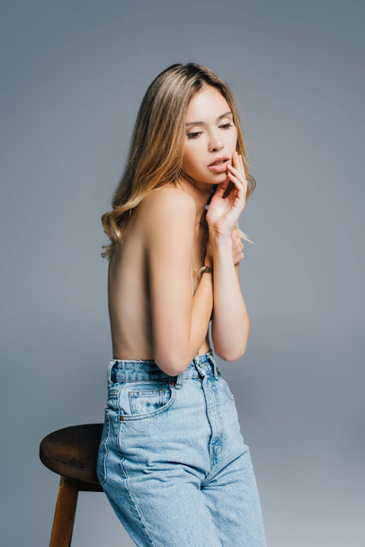 topless, mulher sensual em jeans jeans escondendo seios com as mãos isoladas no cinza - Foto, Imagem