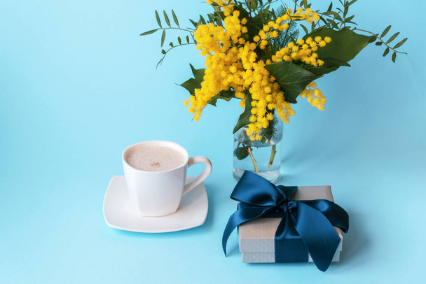 Tasse de café, cadeau dans une boîte et fleurs jaunes de printemps sur un fond bleu. Concept de Saint-Valentin ou de jour des femmes. - Photo, image