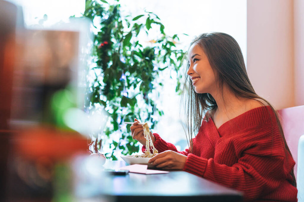 Mooie glimlachende jonge aziatische vrouw in rode kleren eten aziatisch eten in Chinees Vietnamees restaurant - Foto, afbeelding