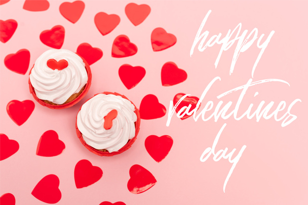 bovenaanzicht van rode harten en cupcakes in de buurt van gelukkige Valentijnsdag belettering op roze - Foto, afbeelding