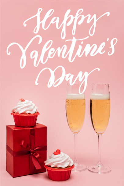 champagne glasses near gift box, cupcakes and happy valentines day lettering on pink - 写真・画像
