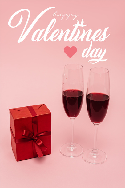 Rotwein im Glas neben Geschenk und fröhlicher Valentinstag Schriftzug auf rosa - Foto, Bild