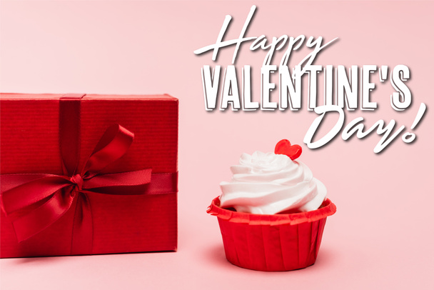 gustoso cupcake con cuore rosso vicino regalo e felice giorno di San Valentino lettering su sfondo rosa - Foto, immagini