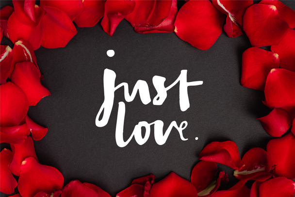 top view of just love lettering in frame with rose petals on black - Foto, afbeelding