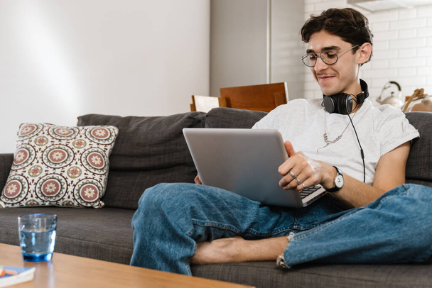 Picture of positive handsome man indoors at home using laptop computer - Valokuva, kuva