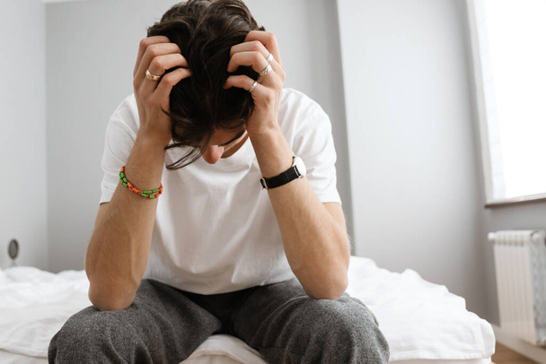 Image of stressed negative man sitting on bed indoors at home - Foto, Imagem